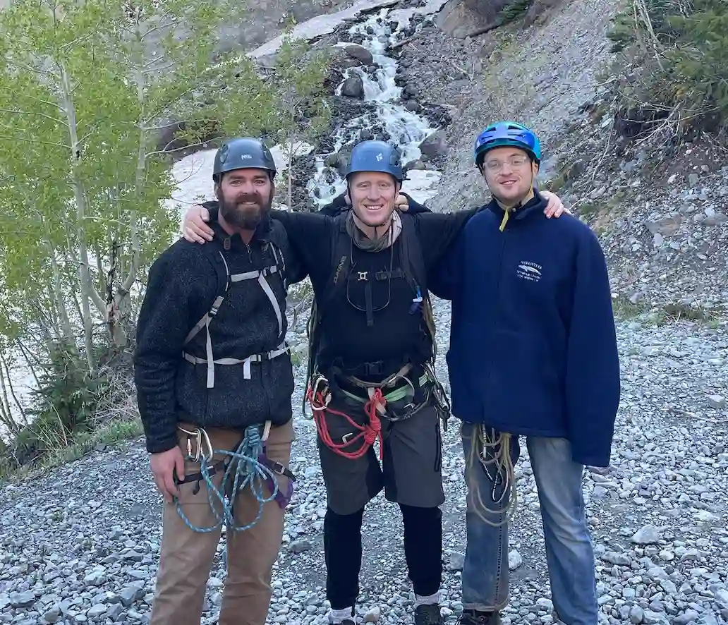 Three men posing in front of a mountain with climbing gear on
