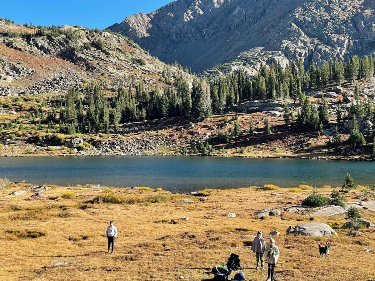 Backpackers stopped beside an alpine lake below a rocky ridgeline in the Holy Cross Wilderness, Colorado